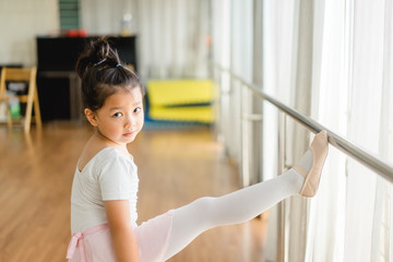 Little ballerinas in ballet studio.Cute little asian girl in a leotard and skirt lifting her leg during a ballet dance class.
