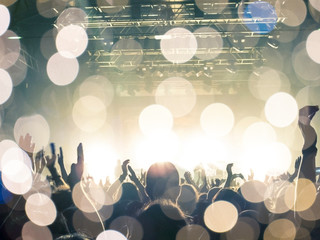 Photo of a concert hall with people silhouettes clapping in front of a big stage lit by spotlights....