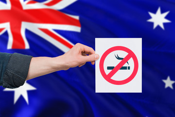Australia health concept. Hand holding paper with no smoking sign over national waving flag. Quit...