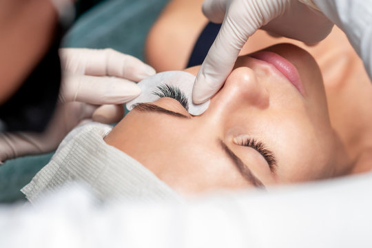Master extends the eyelashes of the client in a beauty salon, eyelash extension procedure, close up.
