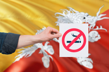 Bhutan health concept. Hand holding paper with no smoking sign over national waving flag. Quit...