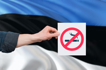Estonia health concept. Hand holding paper with no smoking sign over national waving flag. Quit...