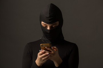 Unknown woman in a black mask with a phone in her hands on a gray background