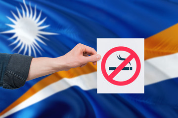 Marshall Islands health concept. Hand holding paper with no smoking sign over national waving flag....