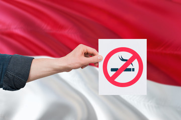 Monaco health concept. Hand holding paper with no smoking sign over national waving flag. Quit...
