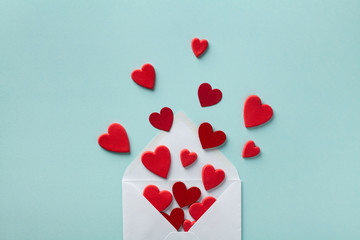 Valentine day greeting concept. Envelope and red hearts on blue background top view. Flat lay.