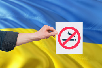 Ukraine health concept. Hand holding paper with no smoking sign over national waving flag. Quit...