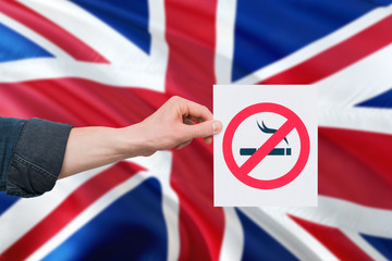 United Kingdom health concept. Hand holding paper with no smoking sign over national waving flag....