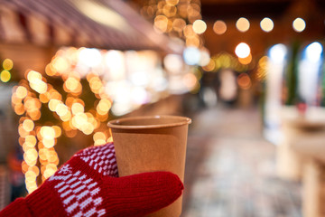 Hand holding a cup of mulled wine with blurred background of winter wonderland, a Christmas Market in European small city