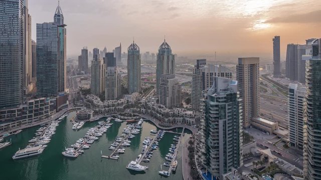 Aerial top view of Dubai Marina night to day transition timelapse. Promenade and canal with floating yachts and boats before sunrise in Dubai, UAE. Illuminated modern towers and traffic on the road