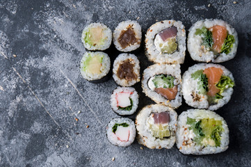 Different sushi on a dark textured background, fresh futomaki, uramaki and hosomaki.