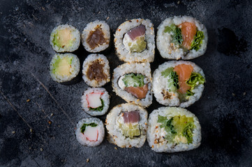 Different sushi on a dark textured background, fresh futomaki, uramaki and hosomaki.