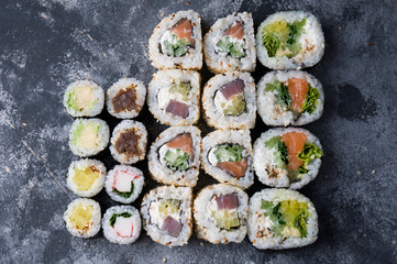 Different sushi on a dark textured background, fresh futomaki, uramaki and hosomaki.