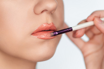 Makeup artist paints lips of client woman lipstick on a brush