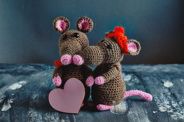 Lovely handcrafted amigurumi mouse holding a pink heart when another knitted toy mouse hugs. Valentine day, February 14, love, relations concept.