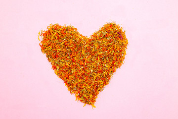 Dried calendula in the shape of a heart on a pink background. Flat lay