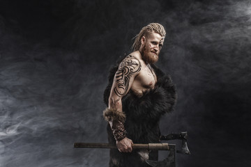 Medieval warrior berserk Viking with tattoo with axes attacks enemy. Concept historical photo