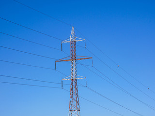 Red white electricity pylon against blue sky on a beautiful sunny day.