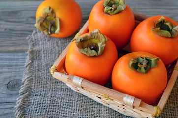 Fresh ripe organic Persimmon or Kaki fruit in a basket on old wooden table.Diospyros kaki.Healthy food vegetarian or raw diet concept.Selective focus.