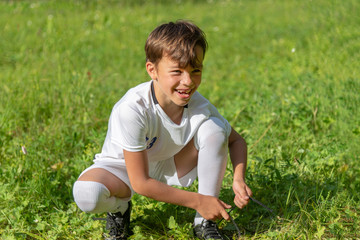 boy on the grass in football uniform tying the lace on his shoe