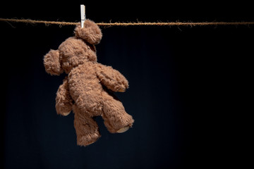 A teddy hangs on an ear, attached to a clothesline with just a clothespin. The background is black.