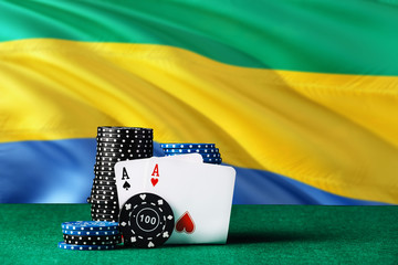 Gabon casino theme. Two ace in poker game, cards and black chips on green table with national flag...