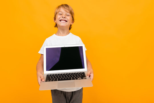 european boy holds laptop screen forward with mockup on orange studio background with copy space