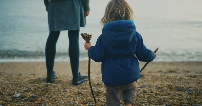 Young mother standing on the beach with her toddler on cold day