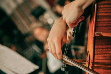Symphony orchestra on stage, hands playing cello. Shallow depth of field, vintage style.
