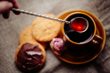 Mixing black tea with vintage bar spoon. Oat cookies with chocolate paste and cup of tea is out of...