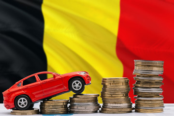 Belgium savings concept. Money for new automobile, toy car and coin piles standing on national flag background. Copy space for text.
