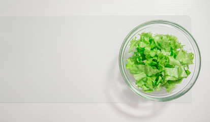 Transparent bowl with green salad on a white table, top view, copy space