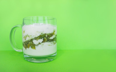Homemade yogurt with kiwi in a transparent cup on green background. Healthy breakfast and food, detox concept. Copy space, place for text