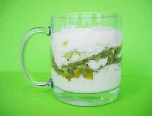 Homemade yogurt with kiwi in a transparent cup on green background. Healthy breakfast and food, detox concept. 