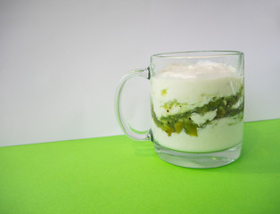 Homemade yogurt with kiwi in a transparent cup on green background. Healthy breakfast and food, detox concept. Copy space, place for text
