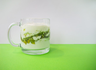 Homemade yogurt with kiwi in a transparent cup on green background. Healthy breakfast and food, detox concept. Copy space, place for text