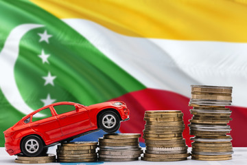 Comoros savings concept. Money for new automobile, toy car and coin piles standing on national flag...