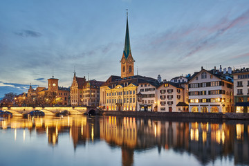 Zürich Altstadt bei Abenddämmerung, Münsterbrücke, Kirchturm Fraumünster und Zunfthaus zur Meisen beleuchtet, Spiegelungen in der Limmat