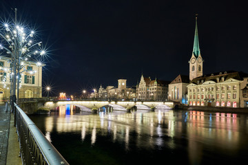Fototapeta premium Münsterbrücke und Fraumünster bei Nacht, Limmatquai mit Weihnachtsbeleuchtung, Spiegelung in der Limmat