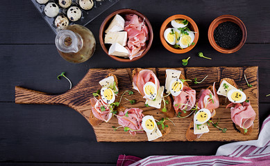 Bruschetta with prosciutto/jamon traditional Italian antipasto. Delicious snack with bread, brie cheese and quails eggs. Health food, tapas. Top view, copy space