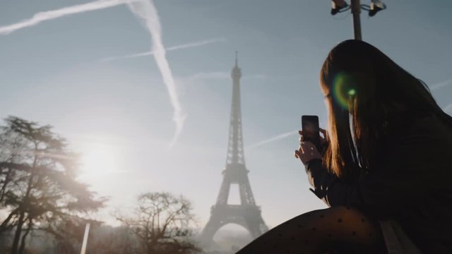 Happy young female blogger taking a picture of sunset Paris Eiffel Tower panorama with phone on vacation slow motion.
