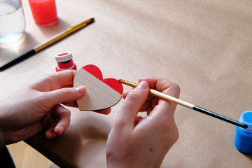 Side view of the female colouring the wooden heart in LGBT pride colours with acrylic paints. Valentine day, masterclass, tutorial, handicraft concept