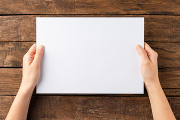 Overhead shot of female hands holding empty paper sheet on rustic wooden background