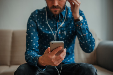 Front view of young man in blue shirt using smartphone with headphones connected - obrazy, fototapety, plakaty