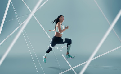 Female athlete running and jumping. Side view shot of healthy woman working out against hi tech background. 