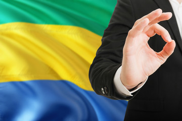 Gabon acceptance concept. Elegant businessman is showing ok sign with hand on national flag...