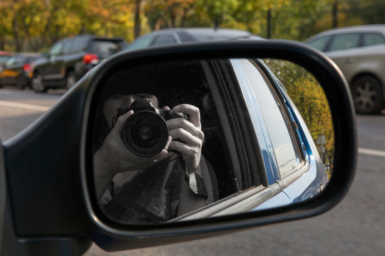 Hidden photographing. Reflection in car mirror of woman with camera. Paparazzi concept