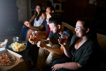 group of friends having fun together watching tv and eating pizza