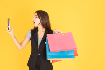 A woman standing on the phone The other hand is carrying a multicolored shopping bag, leaving space to put text in a yellow background.