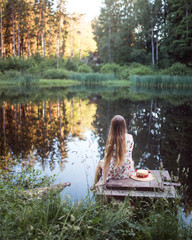 Woman with a straw hat sitting near a pond enjoying a summer day in the forest.
